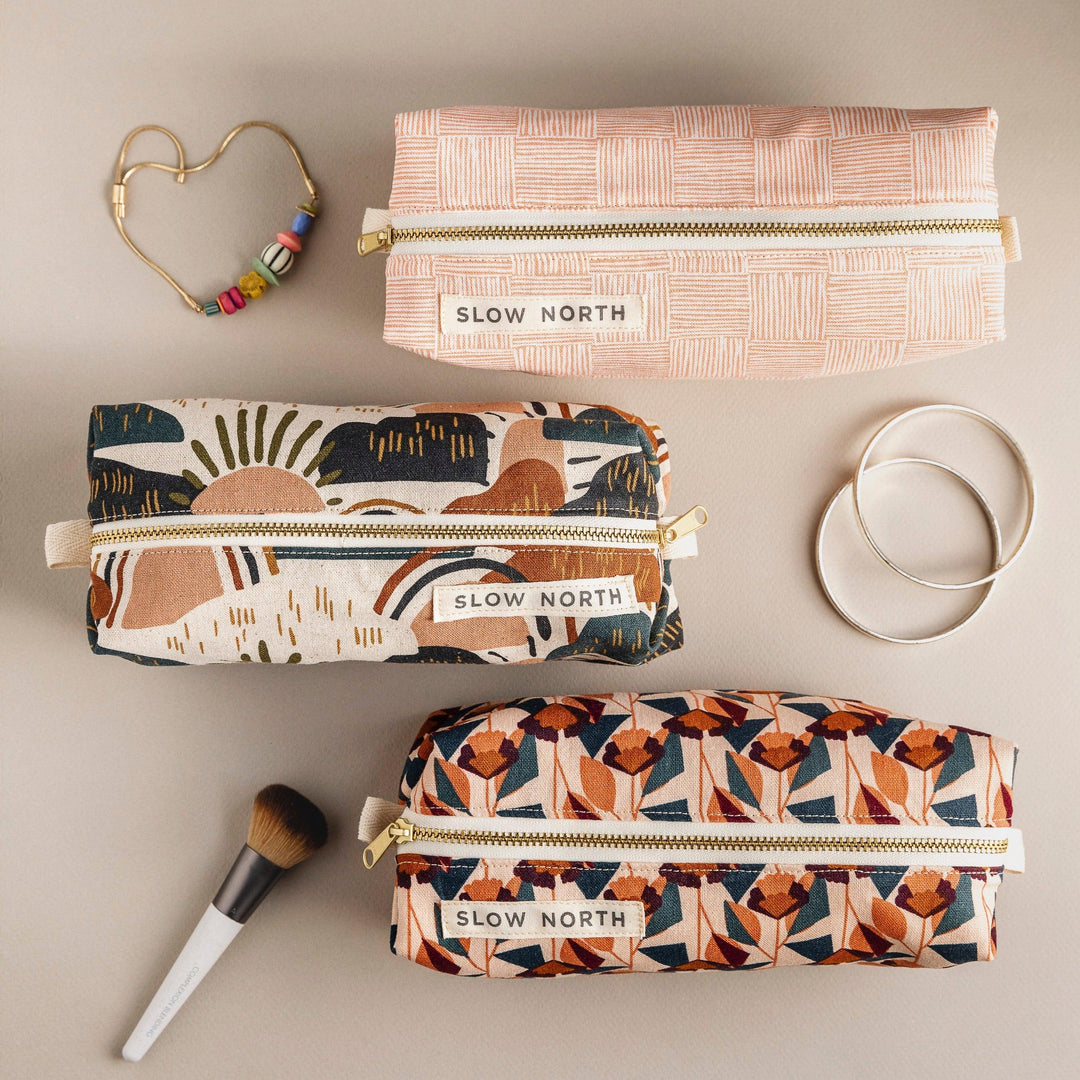 Blush geometric travel pouch among other pouches; gold zipper and label