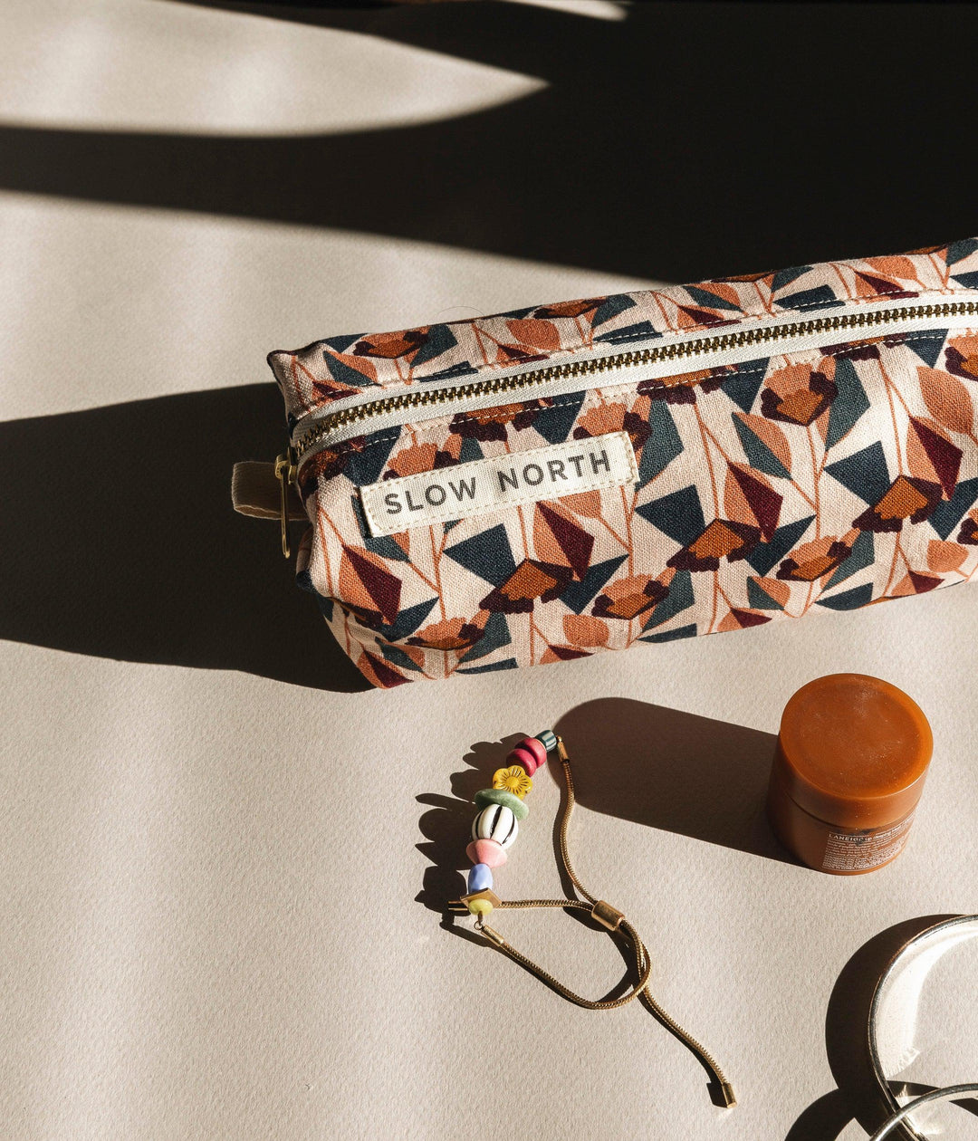 Geometric blush travel pouch with gold zipper, “SLOW NORTH” label, and strap