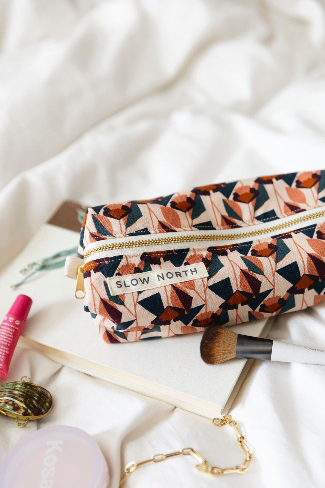 Travel pouch with blush and navy geometric print; gold zipper and “SLOW NORTH” label