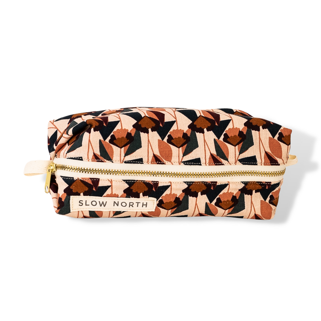 Blush patterned travel pouch with gold zipper, front label, and wrist strap