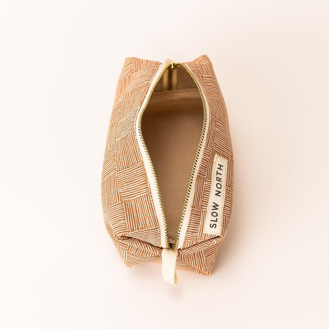 Copper patterned pouch with open zip, gold zipper pull, beige interior lining, side label.