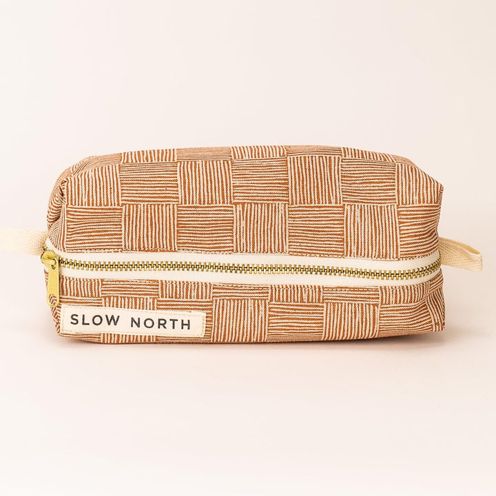 Copper patterned zippered travel pouch with gold zipper and stitched label panel, front view.