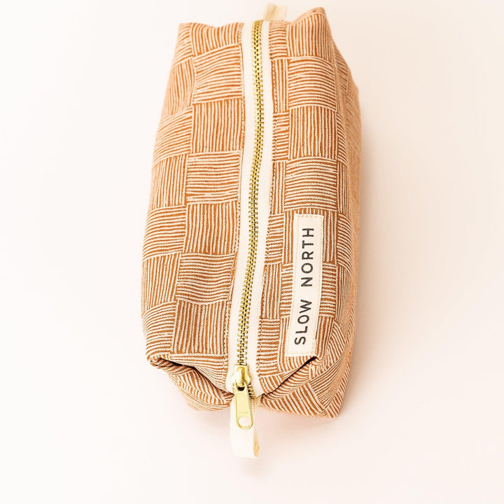 Side view of copper patterned travel pouch with gold zipper, vertical label tape, beige strap.