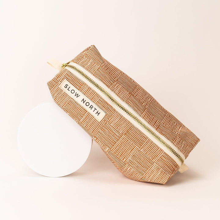 Copper patterned zip pouch with gold zipper tape and label, laid flat with strap visible.