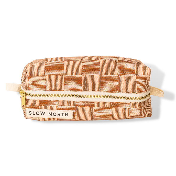 Copper patterned travel pouch with zipper top and beige strap, gold hardware and label.