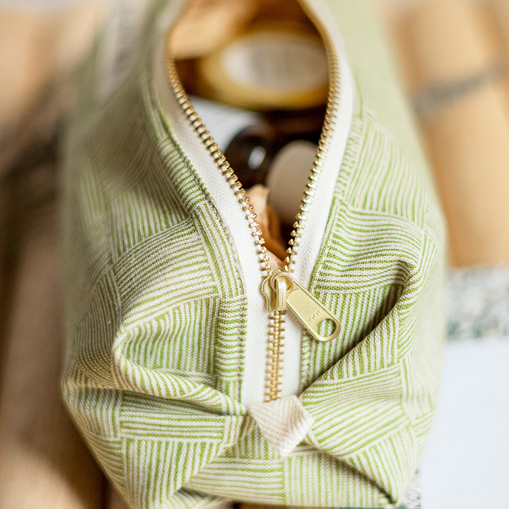 Green woven travel pouch close-up with gold zipper and zipper pull