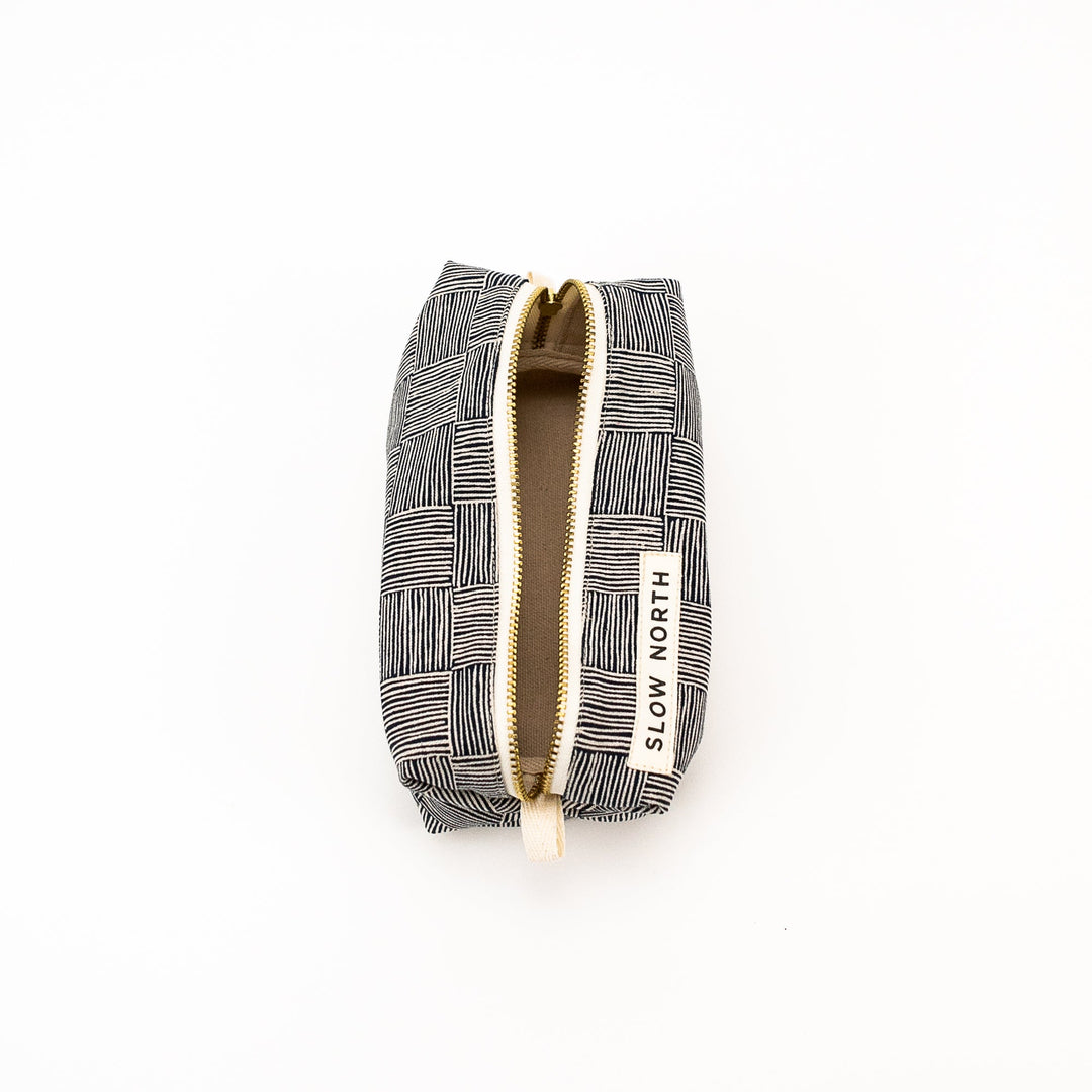 Black-and-white patterned travel pouch with gold zipper tape and hanging strap