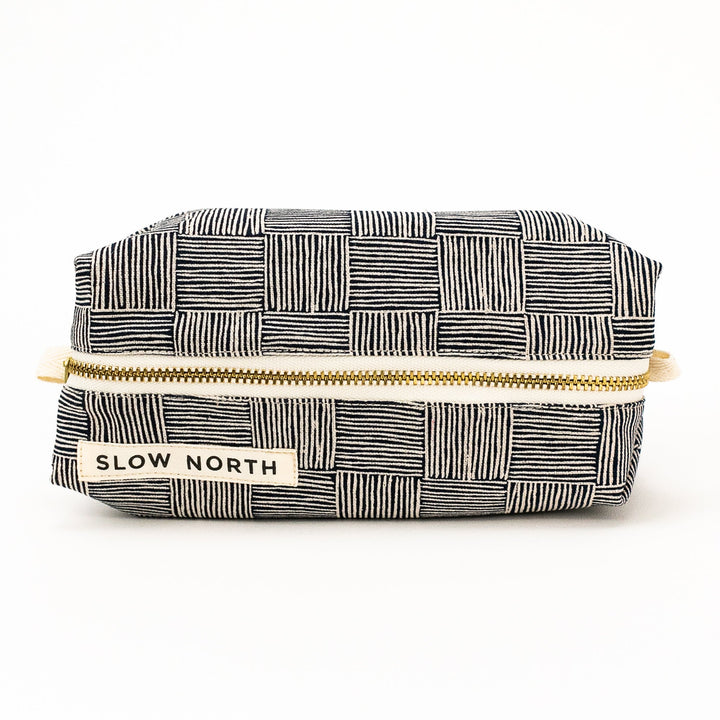 Black-and-white patchwork travel pouch with gold zipper and SLOW NORTH patch