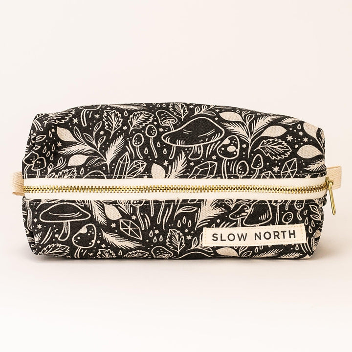 Black patterned travel pouch with gold zipper and “SLOW NORTH” front patch