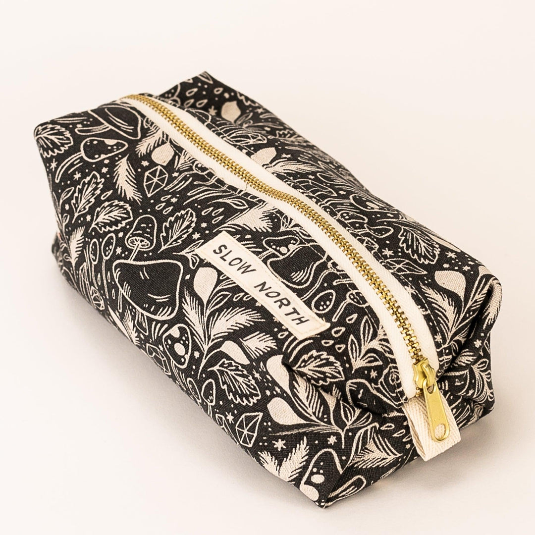 Black patterned travel pouch with gold zipper, angled view of front label