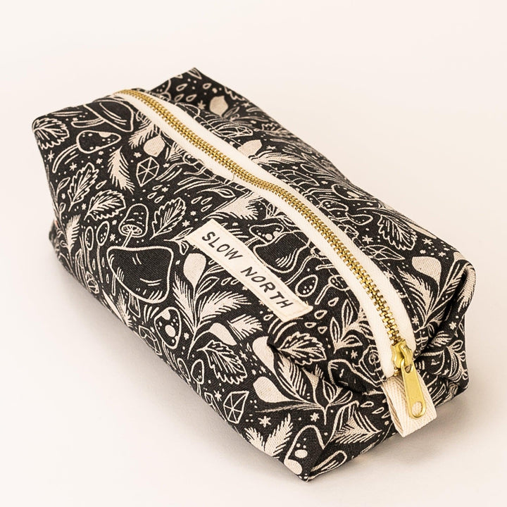 Black patterned travel pouch with gold zipper, angled view of front label