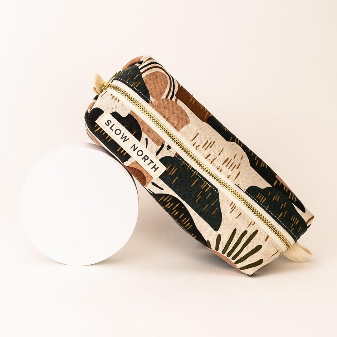 Travel pouch with desert-pattern fabric and gold zipper; beige fabric loop on end