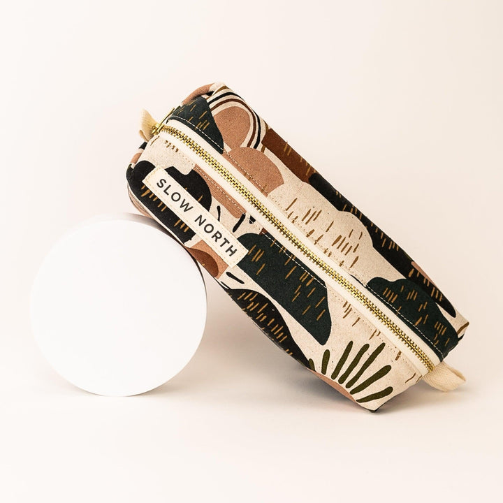 Travel pouch with desert-pattern fabric and gold zipper; beige fabric loop on end