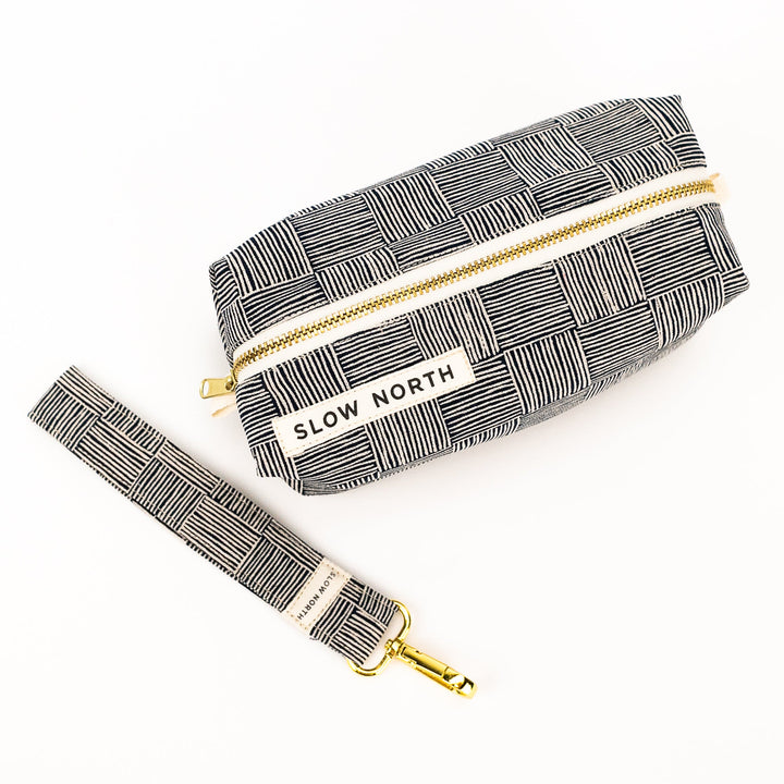 Black-and-white patterned travel pouch with gold zipper pull and adjustable strap