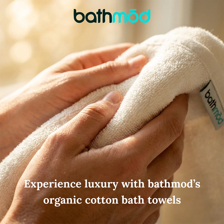 White bath towel close-up with hands touching the textured surface and stitched logo label.