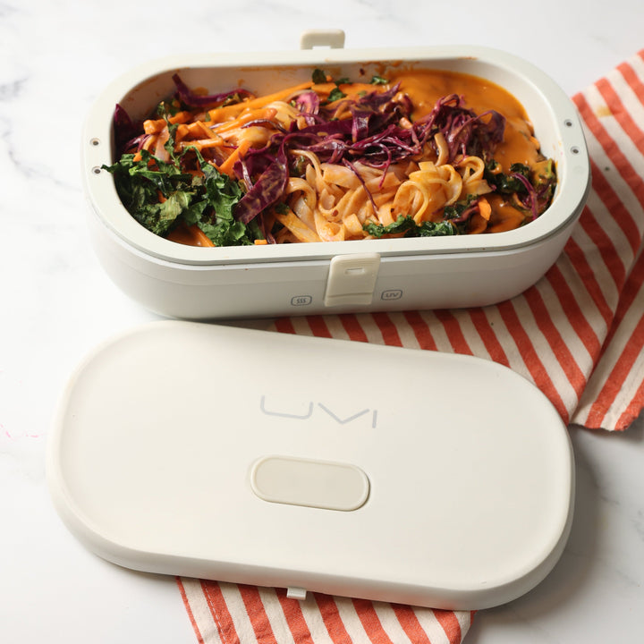 White self-heating lunch box with lid open, filled with pasta and vegetables.