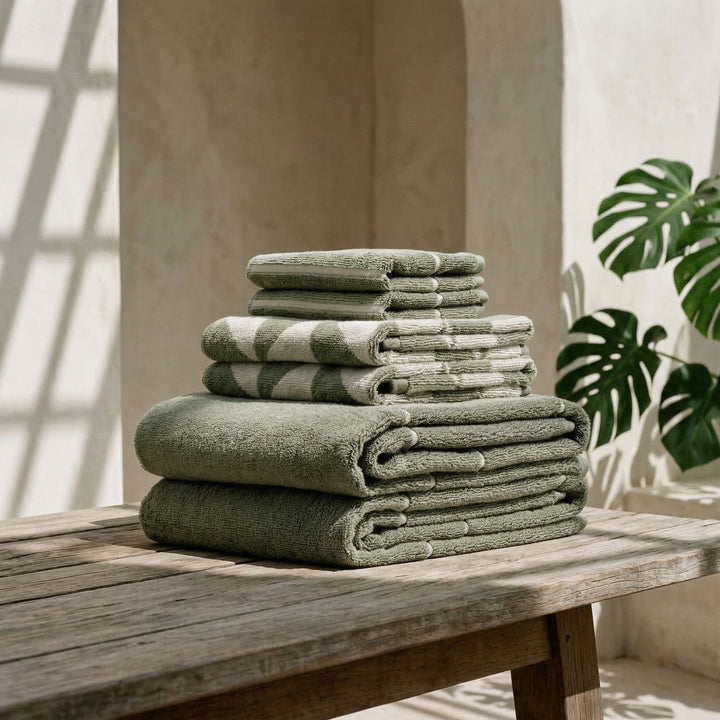 Folded sage green and ecru striped cotton towels stacked with rolled edges