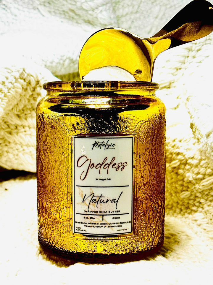 Amber-gold body butter jar with black lid and gold spoon, label reads “Natural”