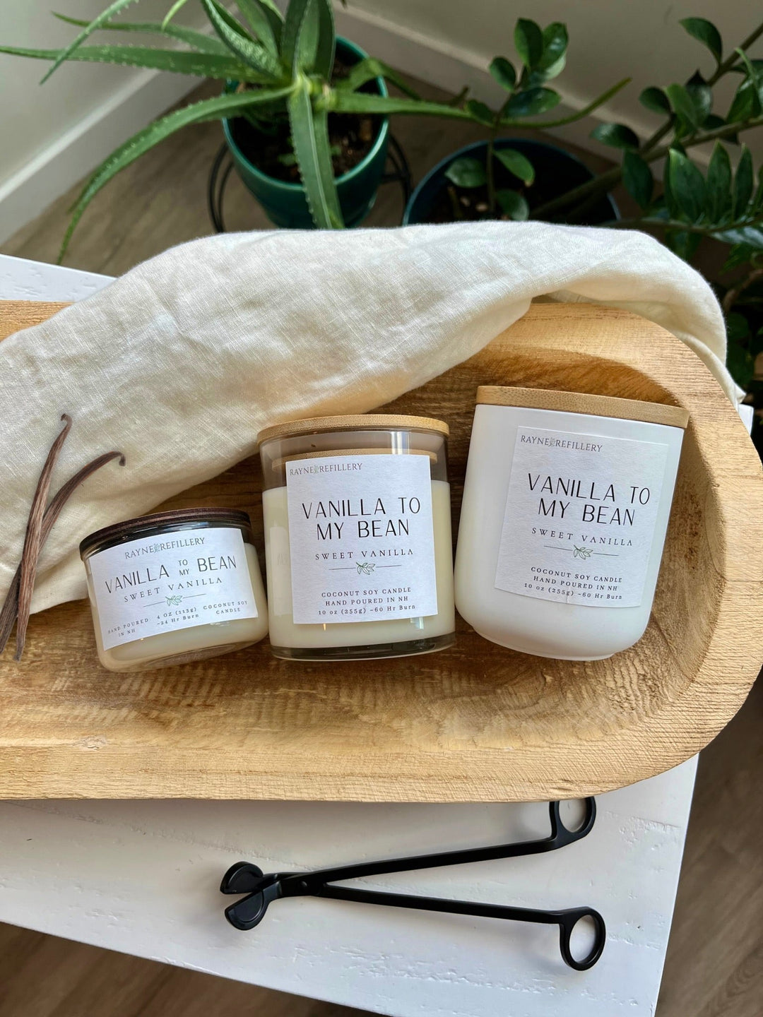 Set of vanilla coconut soy candles in white jars with wooden lids on wooden tray
