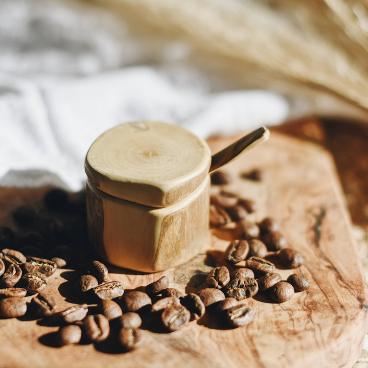Wooden salt box with round lid and wooden spoon beside salt crystals