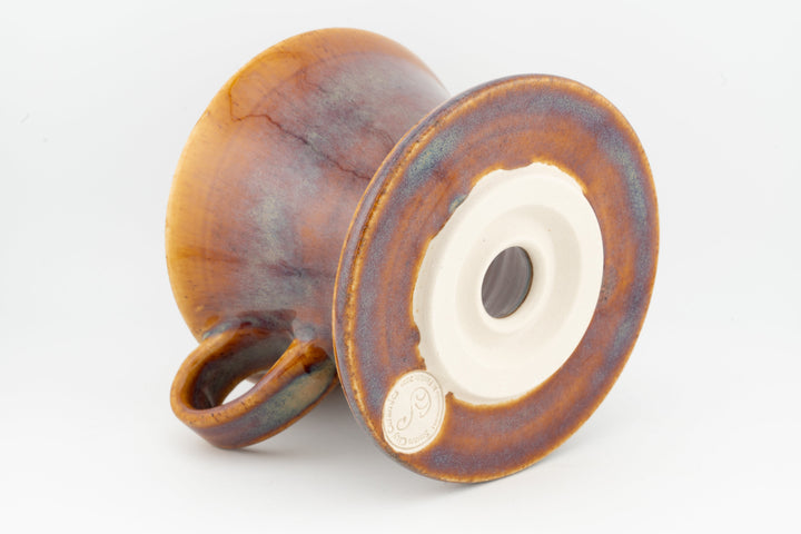V60 ceramic coffee dripper underside with circular vent, amber-brown glaze, side handle.
