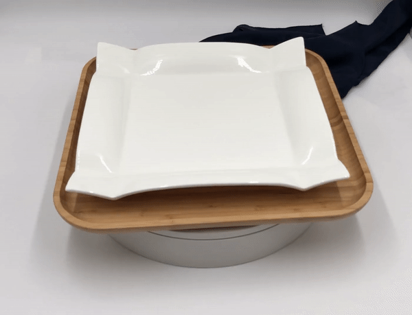 Square white porcelain dinner plate with wide rim on bamboo tray