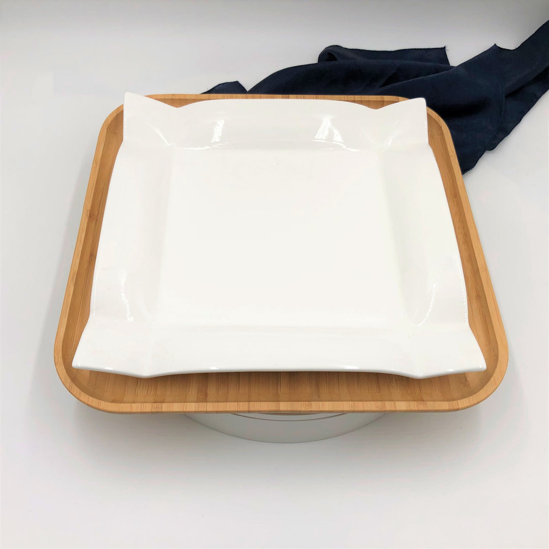 Square white porcelain dinner plate with glossy finish on bamboo tray