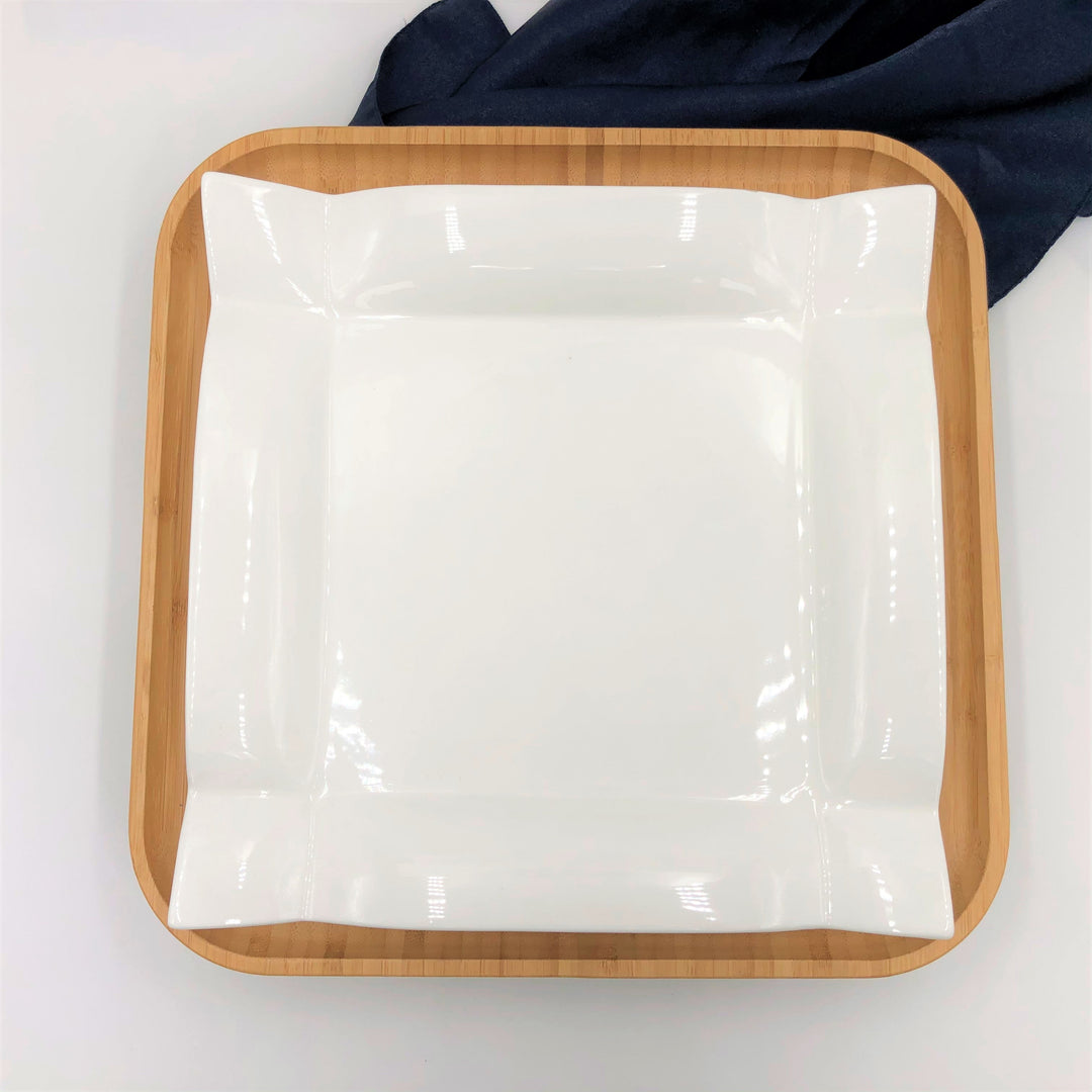 Square white dinner plate with glossy porcelain surface in bamboo tray