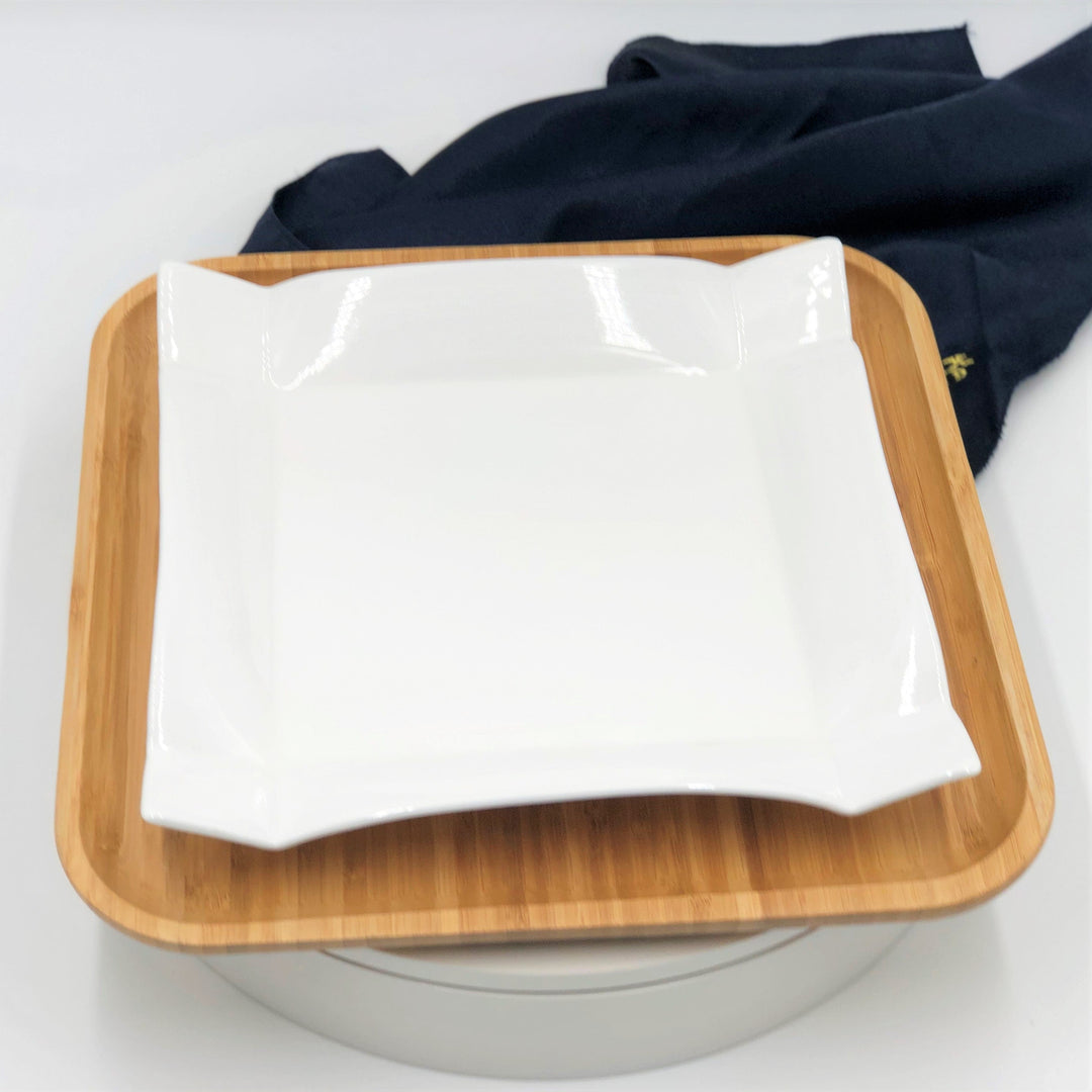 Square white glossy porcelain dinner plate on light wood bamboo tray