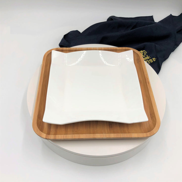 Square white porcelain dinner plate on bamboo serving tray
