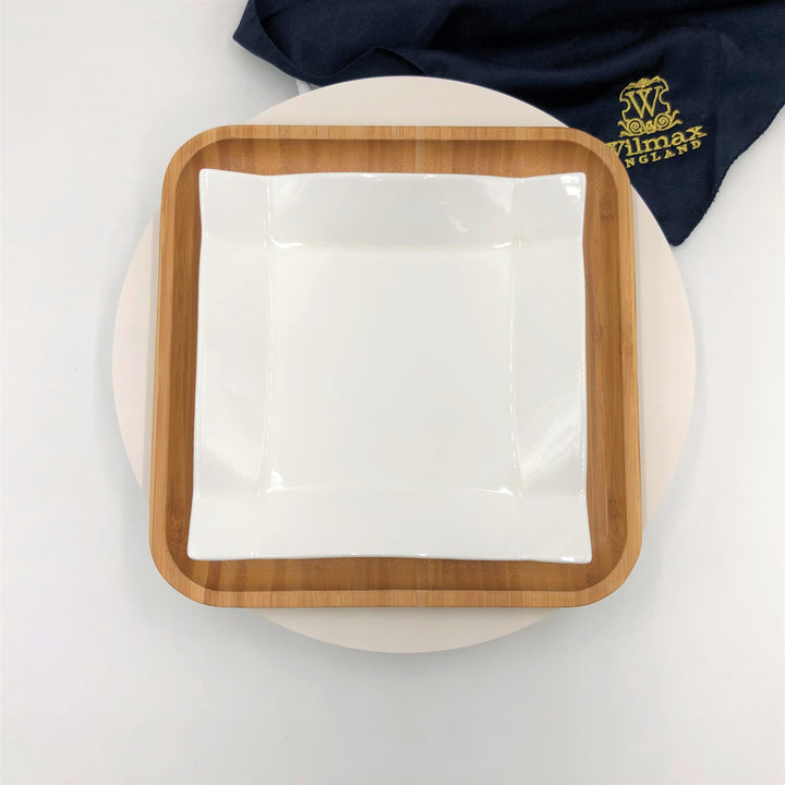 Square white porcelain plate with raised rim on bamboo tray