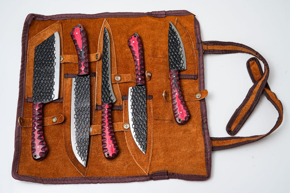 Open leather knife roll holding five dark carbon-steel knives with red diamond handles
