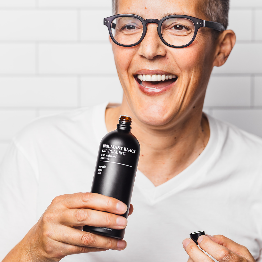 Person holding a Brilliant Black oil pulling charcoal mouthwash bottle