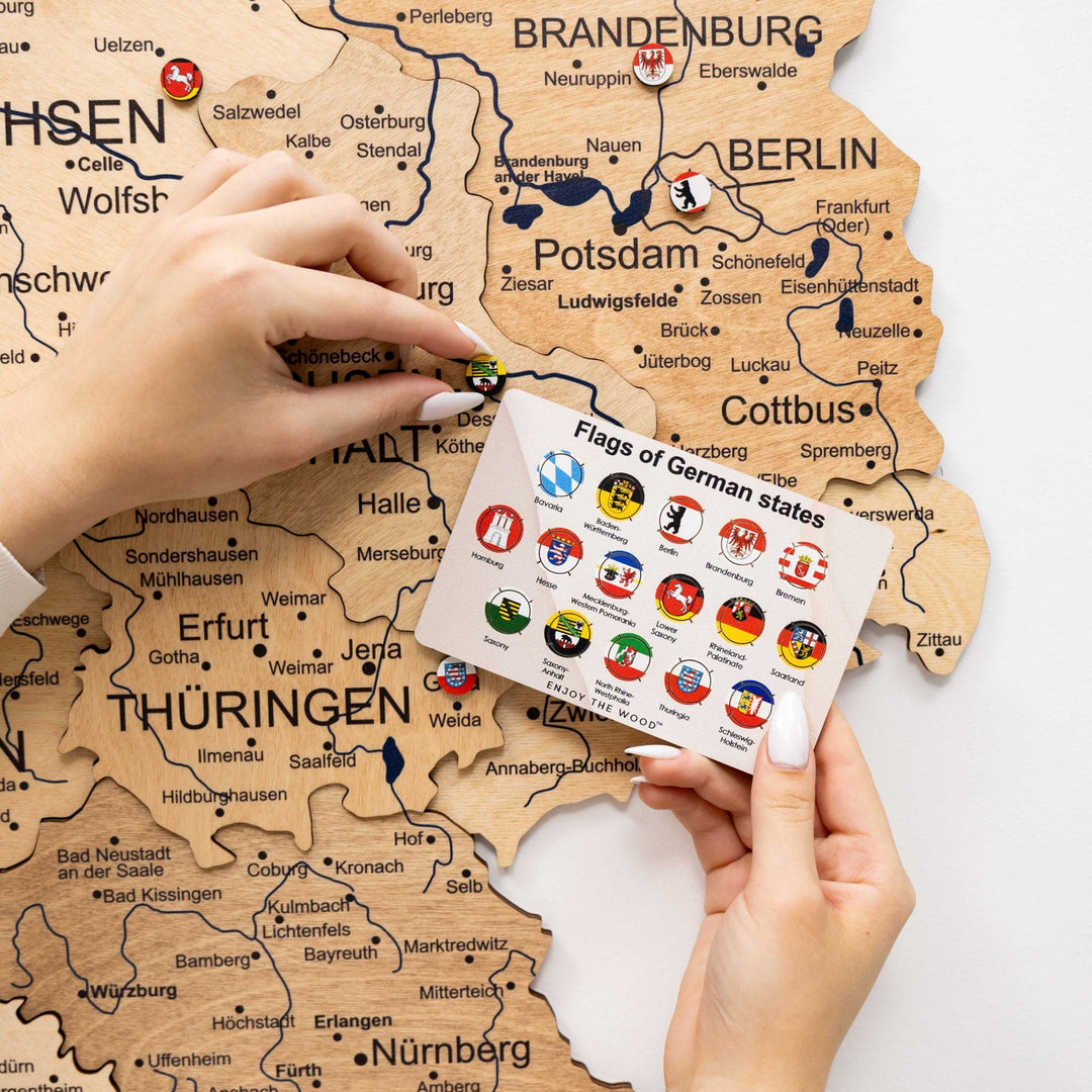 Wooden Germany map with flag stickers and labeled federal states, hands shown