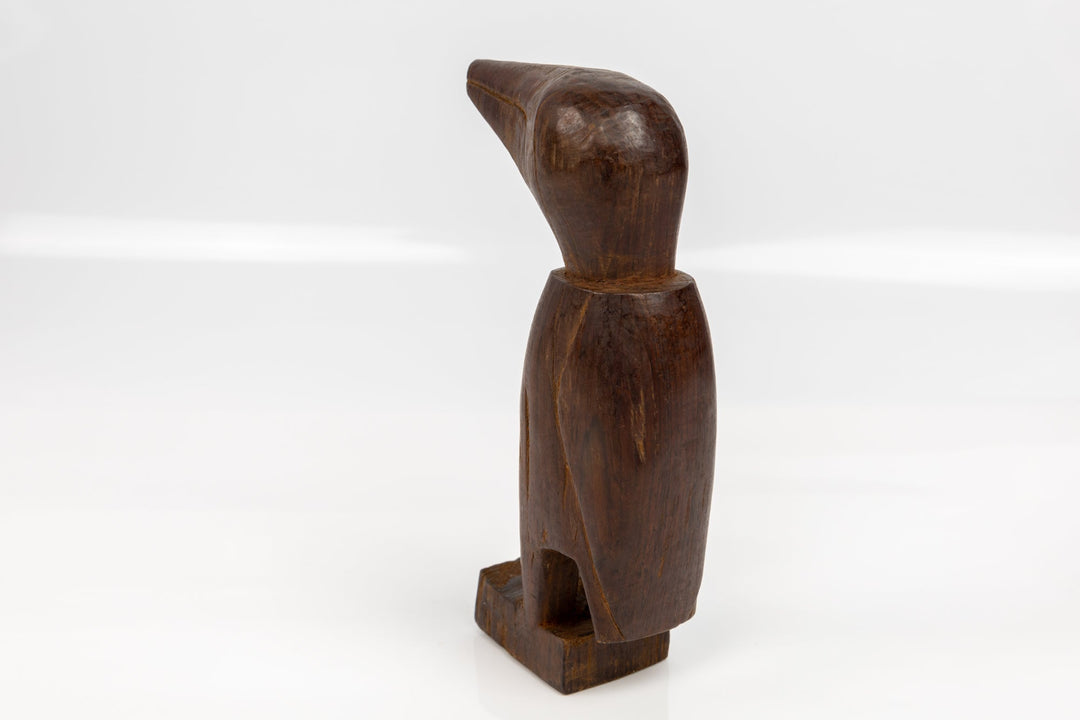 Dark brown wood bird figurine standing with beak angled upward on base.