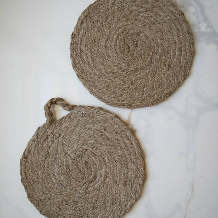 Two round woven natural trivets with handle loops, laid on marble surface