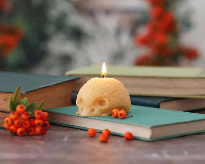 Hedgehog beeswax candle with lit wick, yellow wax on wooden surface