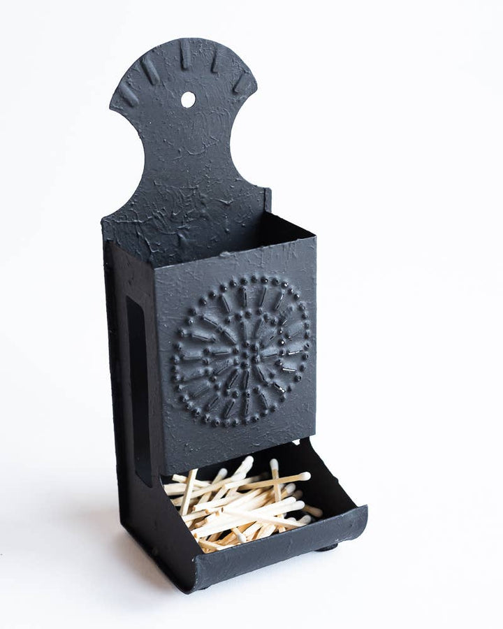 Decorative dark metal matchbox holder with circular embossed emblem and open match slot