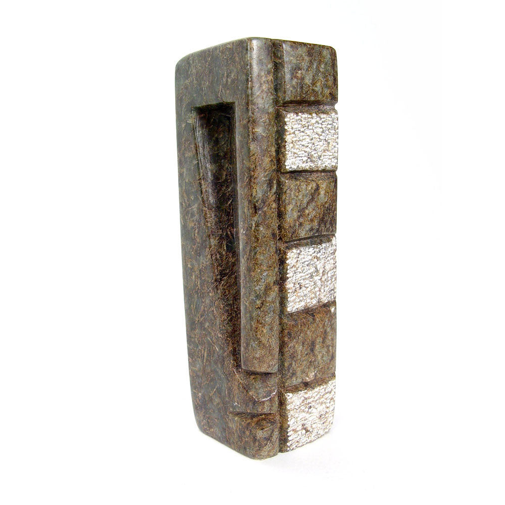 Abstract stone sculpture with face-like grooves and stacked white inlays, side view