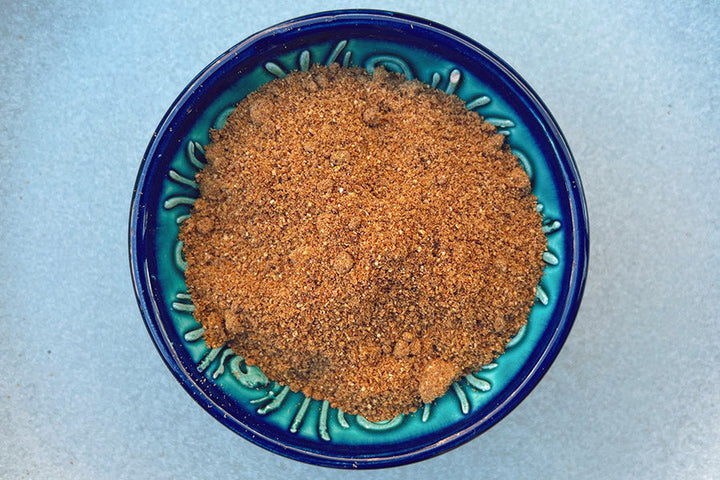 Ground anardana spice in a blue bowl, reddish-brown granules