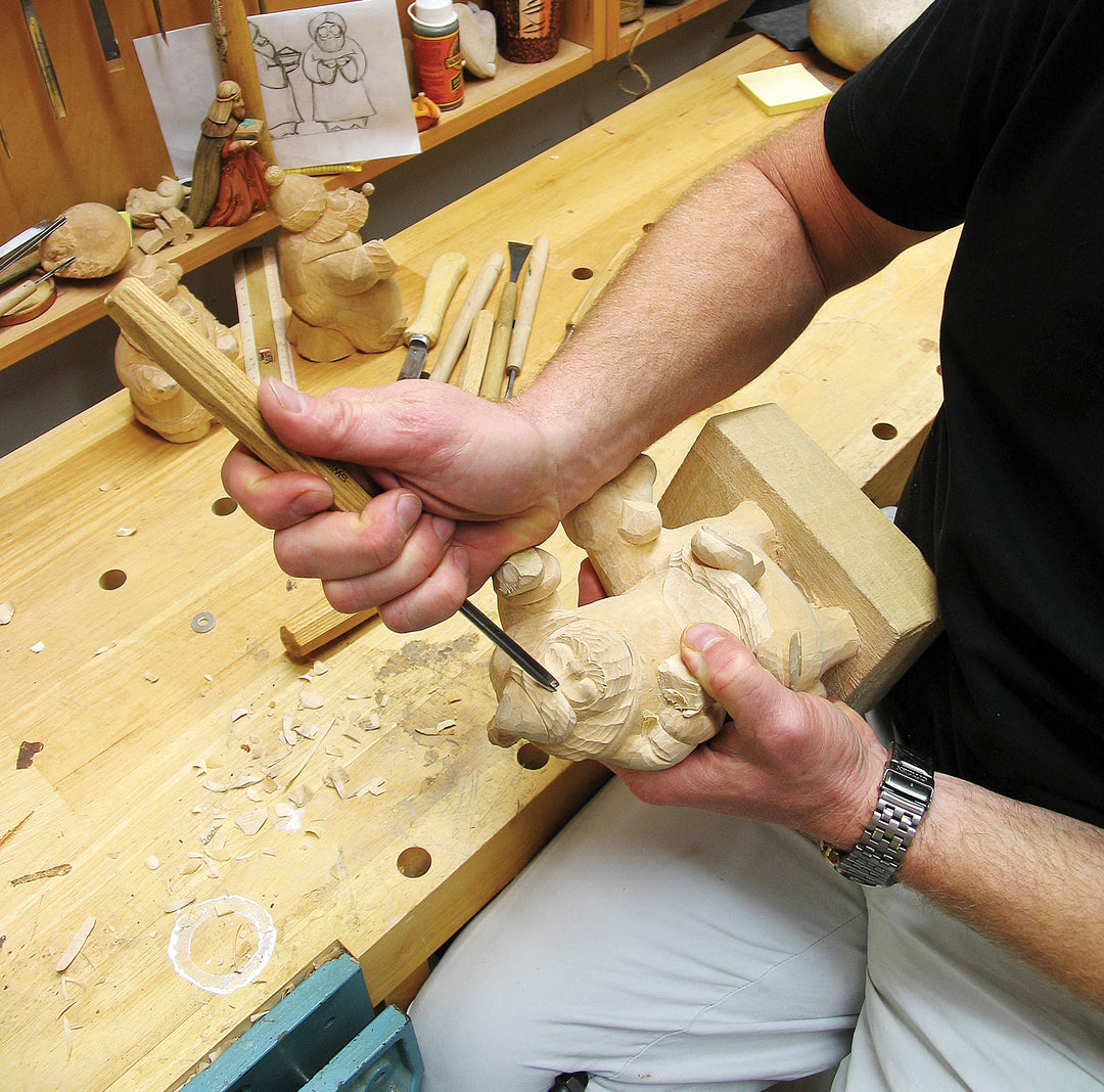 Hands carving a small wooden figure on a workbench, detailed workshop crafting
