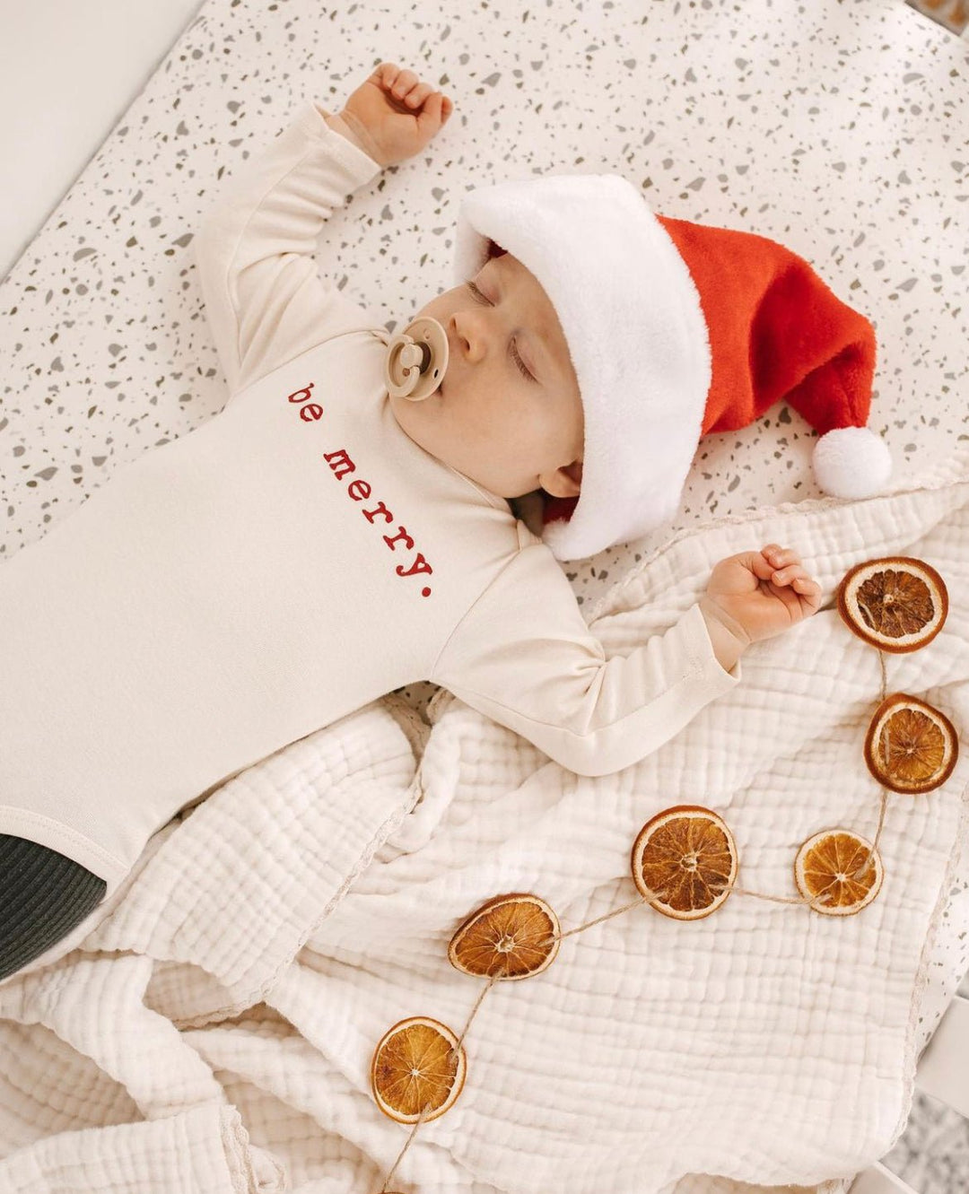 Baby in cream long-sleeve bodysuit with red "be merry" chest print