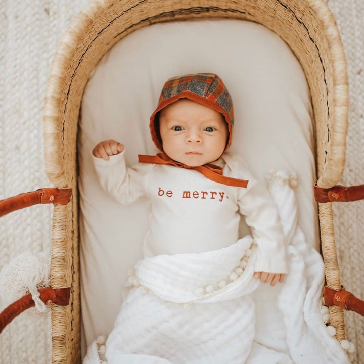 Baby in cream long-sleeve bodysuit with red "be merry" text on chest