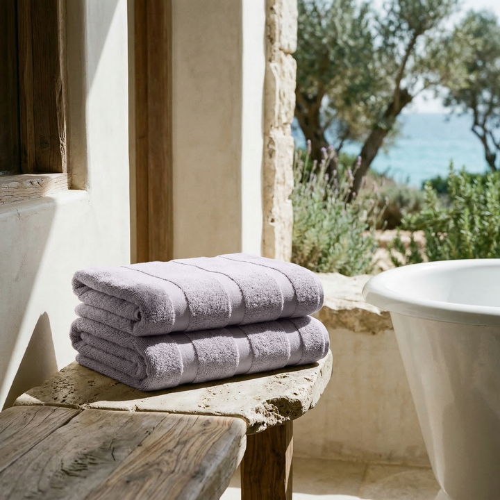 Lilac cotton towels stacked neatly on a ledge beside a bathtub.