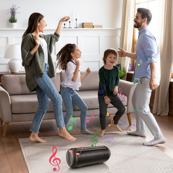 Portable wireless party speaker on floor with family dancing nearby, dark gray.