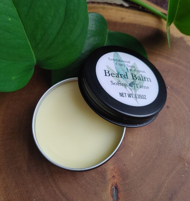 Open round beard balm tin with pale cream balm and black rim, sandalwood scent