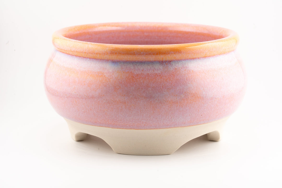 Ceramic bonsai pot in pink-orange glaze with raised rim and three small feet.