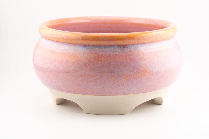 Ceramic bonsai pot in pink-orange glaze with raised rim and three small feet.