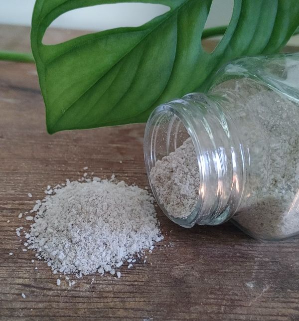 Small glass jar tipped with loose pink clay body soak powder spilled on a surface.