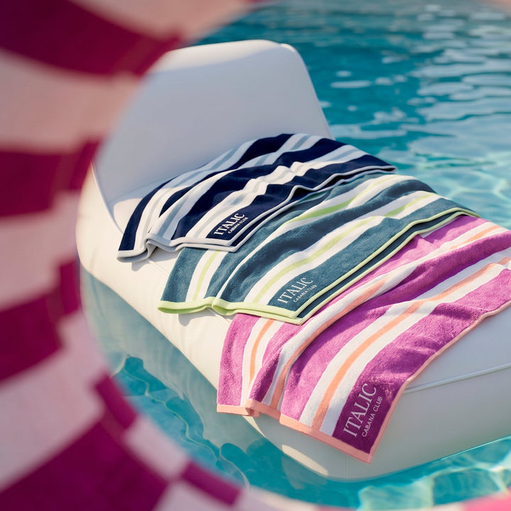 Folded cotton beach towel, multicolor vertical stripes in navy, teal, pink, and white.